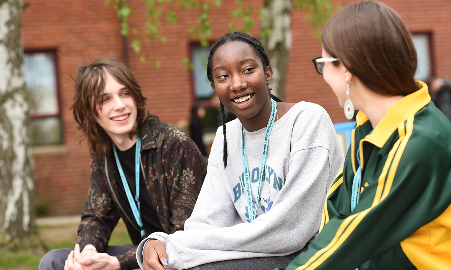 Three students sitting on a bench chatting